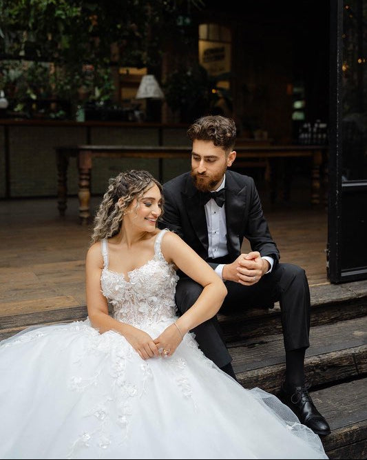Couple in wedding attire sitting on wooden steps outdoors.